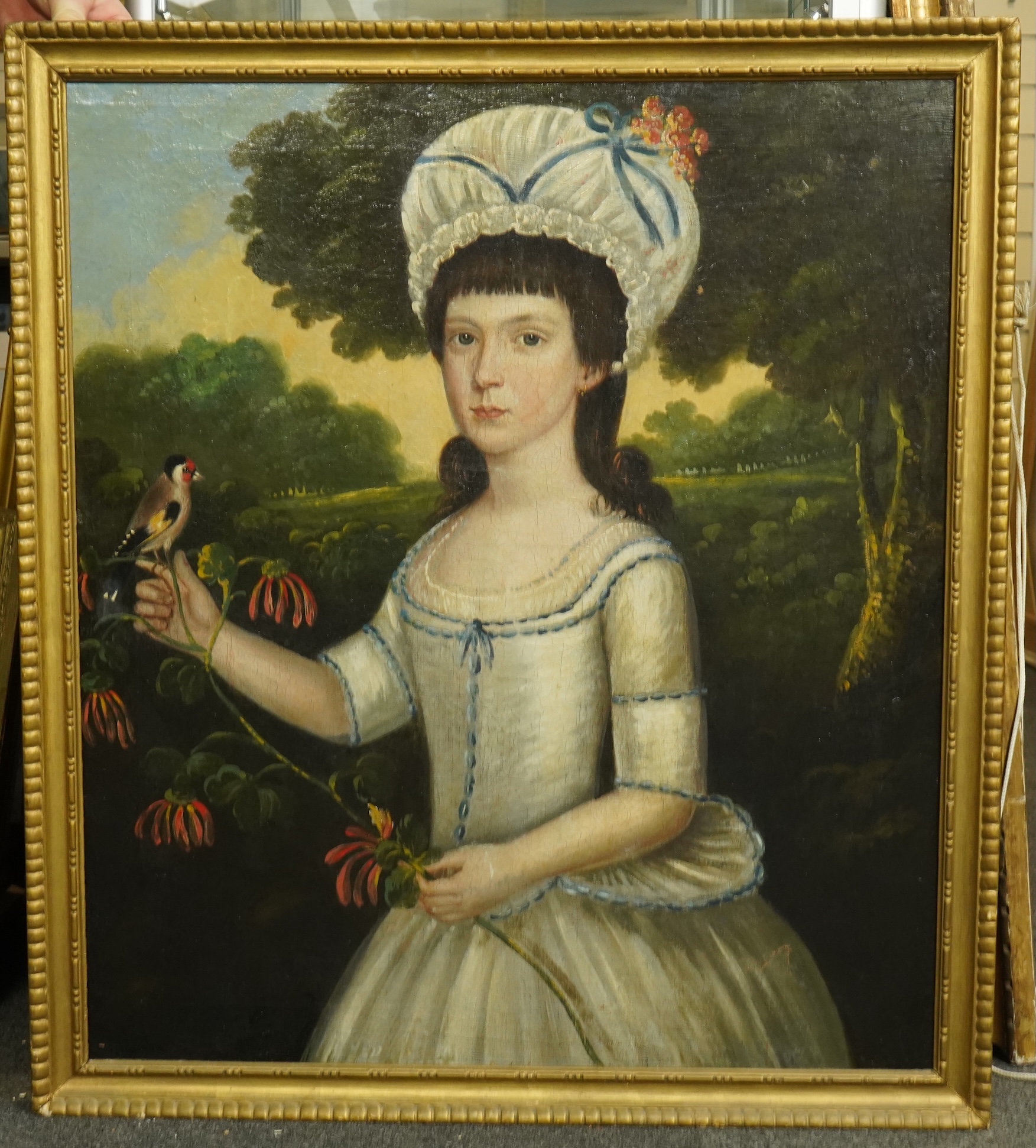 Late 18th century English School, Half length portrait of a young woman, standing in a landscape holding a goldfinch, oil on canvas, 74 x 46cm